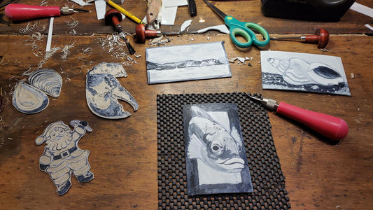 Six new linocut printing plates in progress on my shop counter at Norton's Cove Studio including tools and mess.