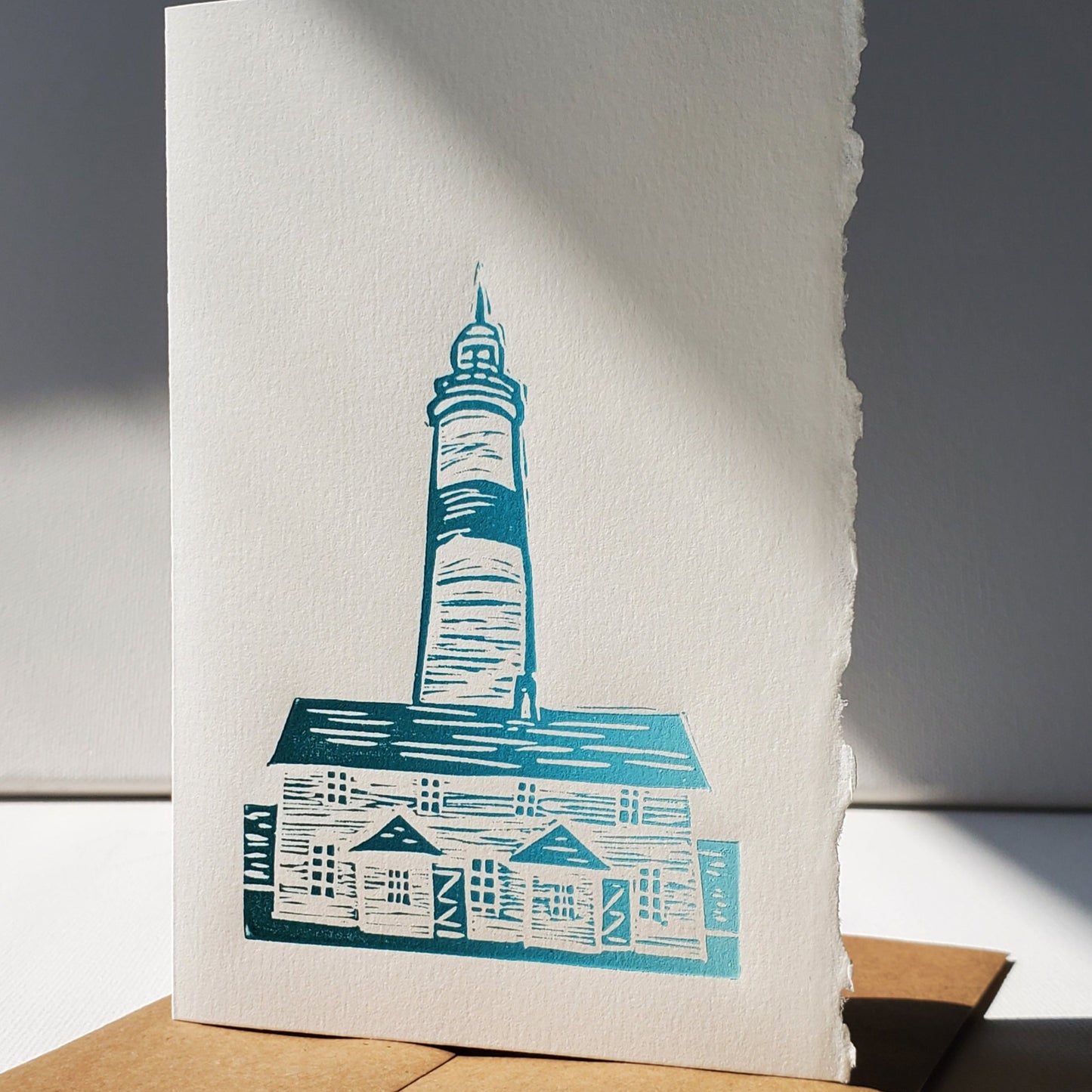 Janet Davis' Linocut image of the Point Amour historic lighthouse shown in green ink on a Kraft envelope.