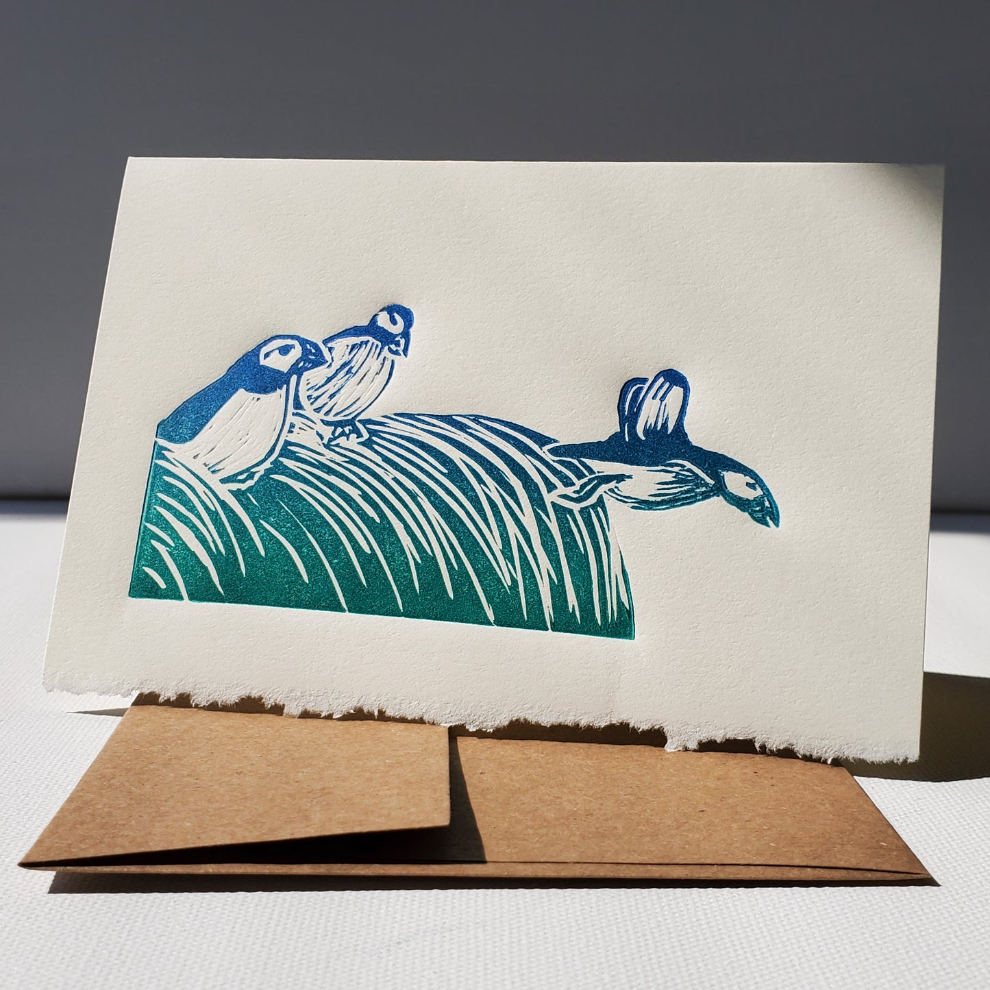 Janet Davis' Puffins linocut printed in a blue-green rainbow roll on a Norton's Cove Card.