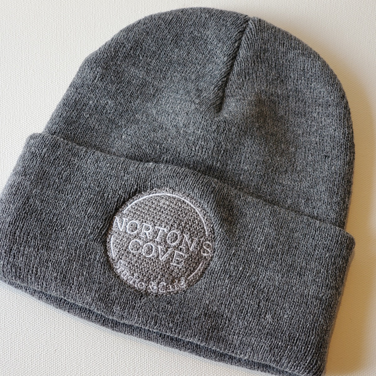 Grey toque with Norton's Cove Studio & Café logo embroidered on the rolled cuff in white thread.