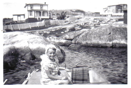 A young girl sitting in a boat in Norton's Cove with Captain Charlie Kean's house in the background.