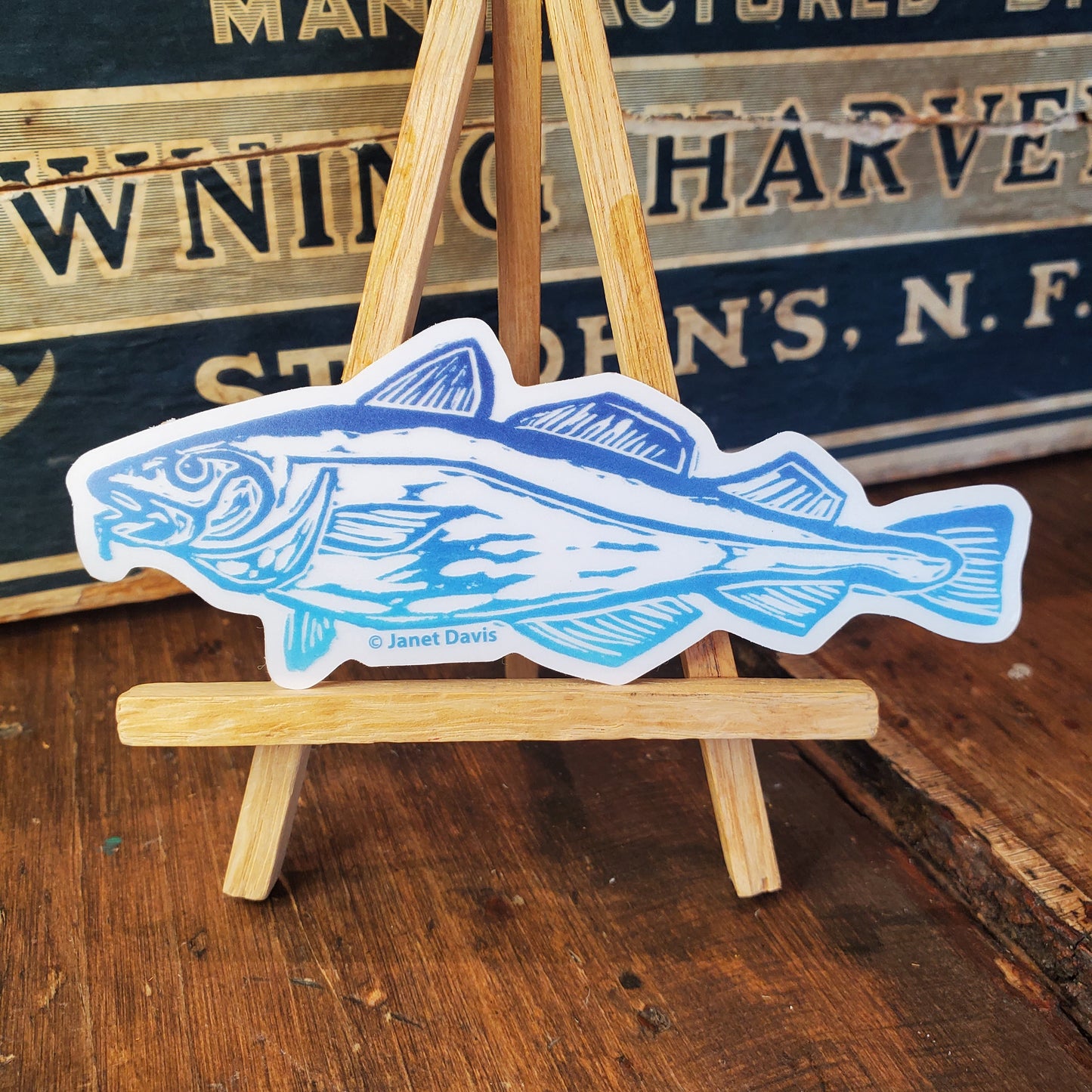 Blue Codfish vinyl sticker on mini easel with old shop counter background.
