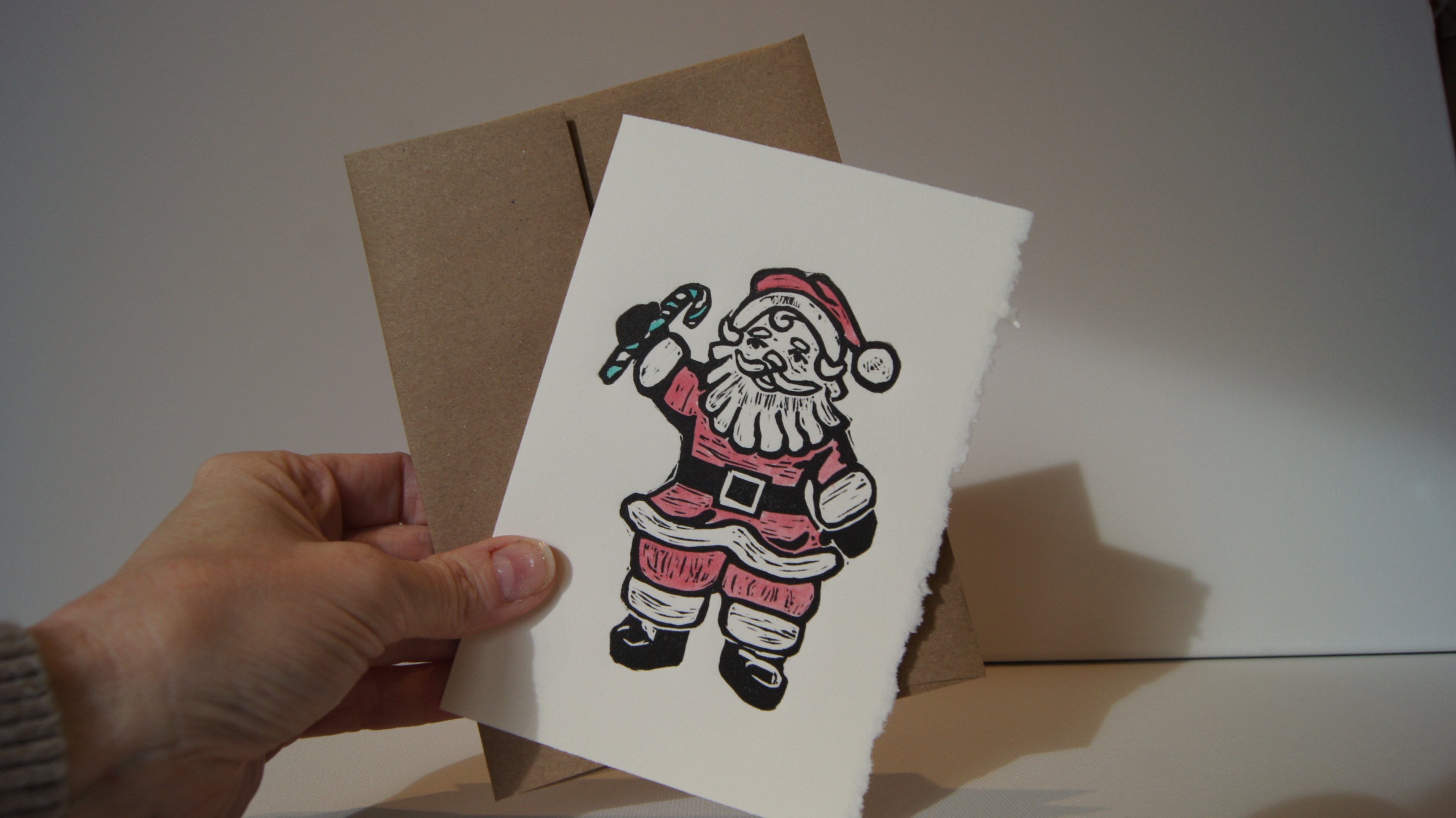 Janet holds a brand new 2025 holiday card: Salty Santa, inspired by a salt + pepper set found at Jenniex House in Norris Point, NL.