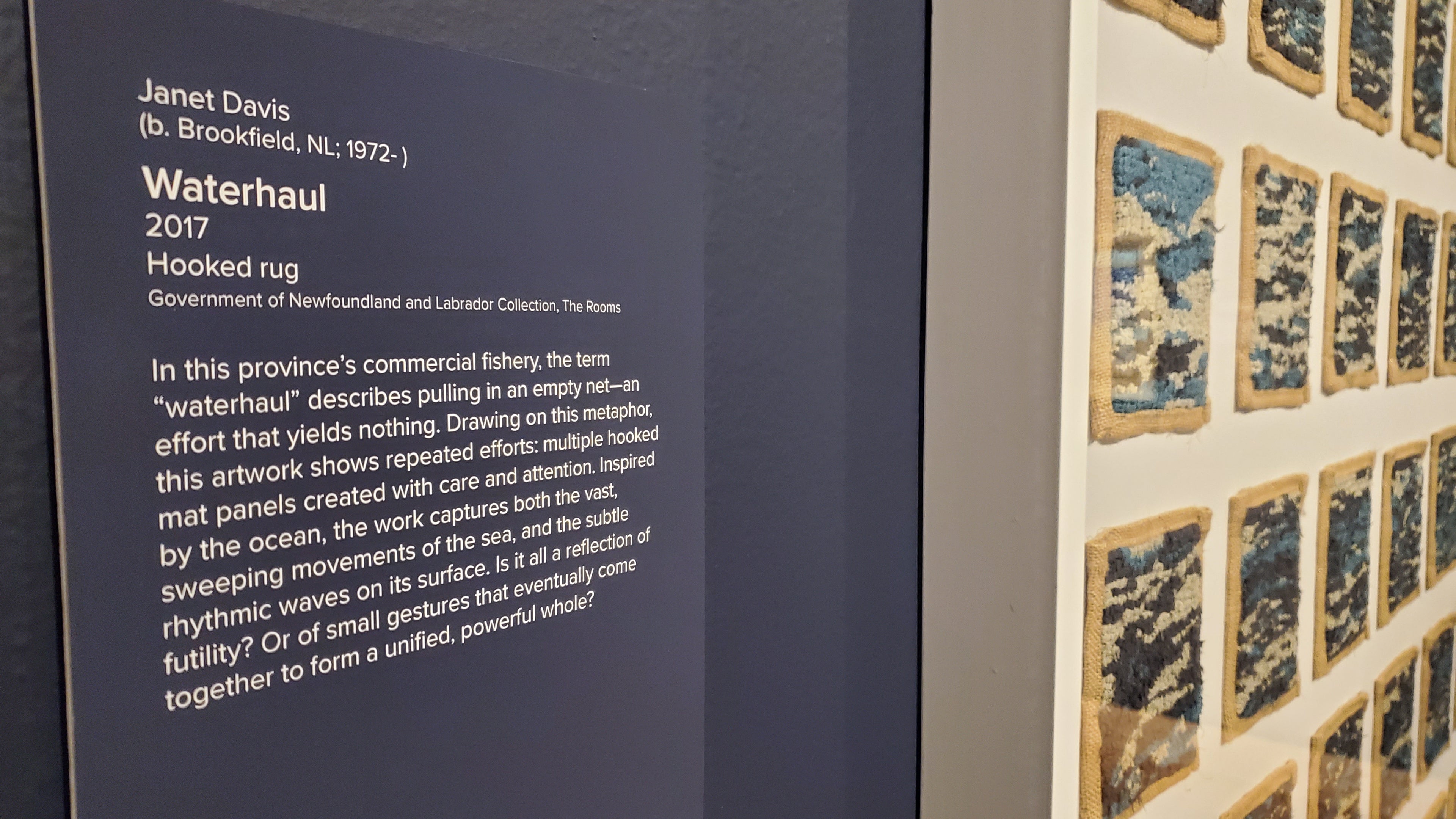 A peek at the framed Waterhaul hooked mat by Janet Davis 2017 as displayed at the art gallery at The Rooms' exhibit Grounded, 2025.  Janet and family were present at the opening event on the 28th of February.