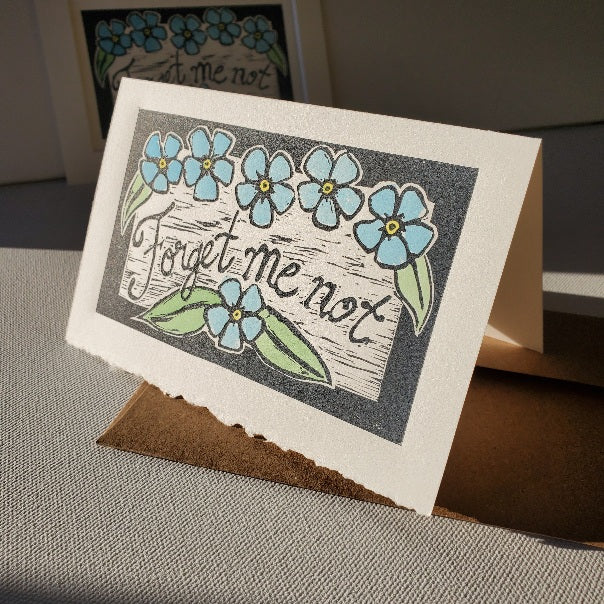 Forget-me-not card printed on antique white paper with a natural decal edge along the bottom front.  Lino-cut print hand tinted with watercolour paints.  cJanetDavis
