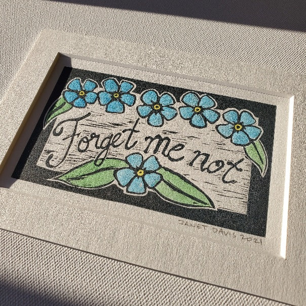 Forget me not lino-cut print with watercolour.  Grey ink and blue, green, and yellow paint on antique white cotton fibre paper and a matching 5x7" mat